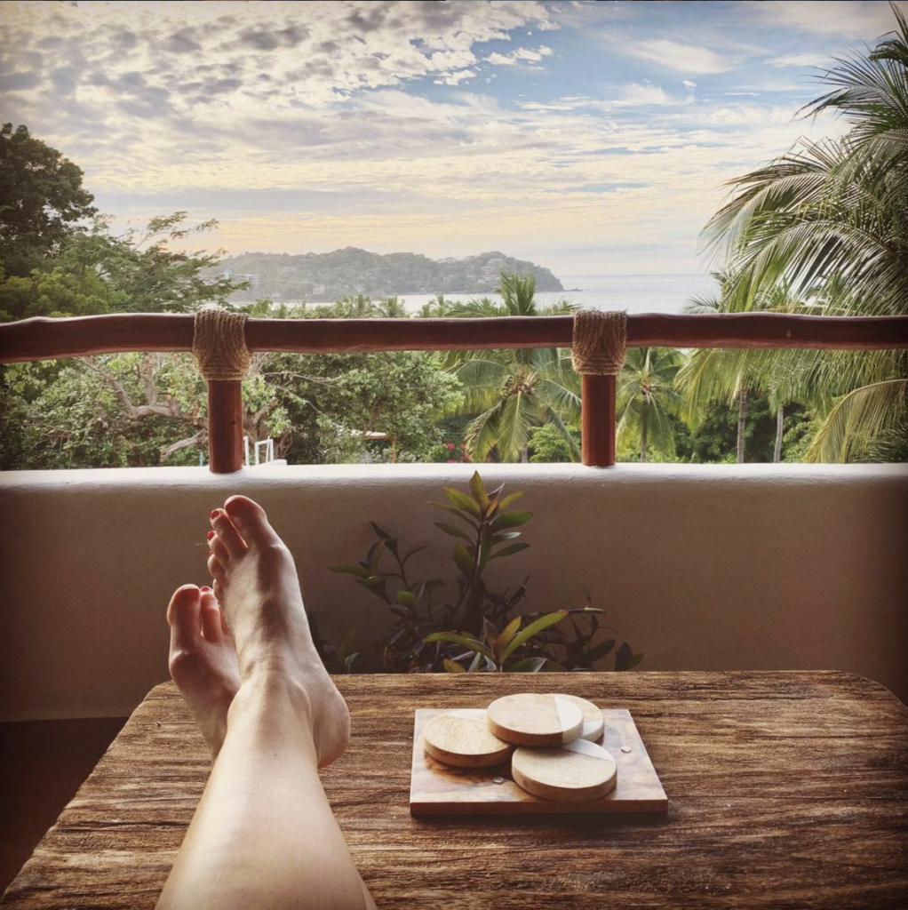 photo taken by one of my clients of her legs on a table on a balcony with a beautiful view of palm trees, the ocean, and hills in the distance. 