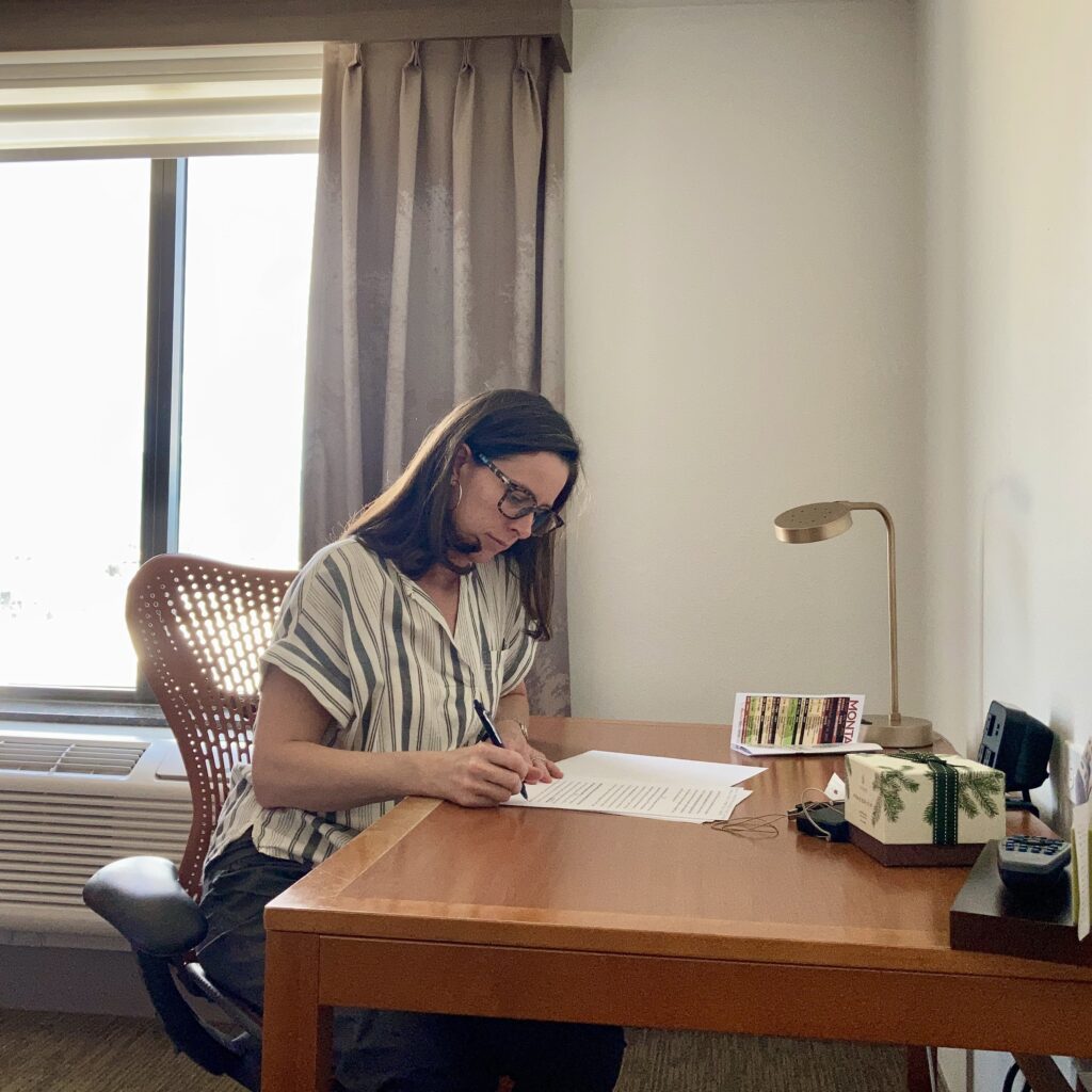 Montana Life Coach Christine Seager sitting inside at a desk writing a letter using pen and paper